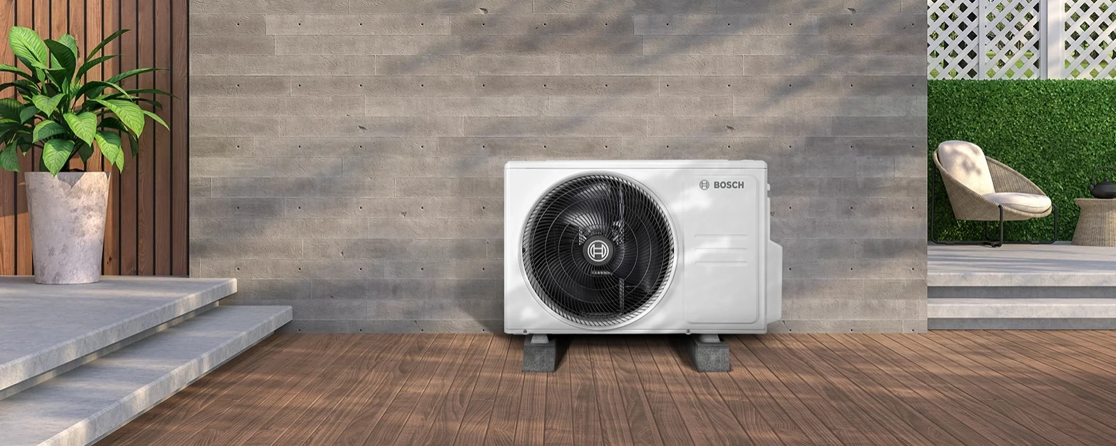 An outdoor air conditioning unit with a built-in fan stands on a foundation in front of the wall of a building.